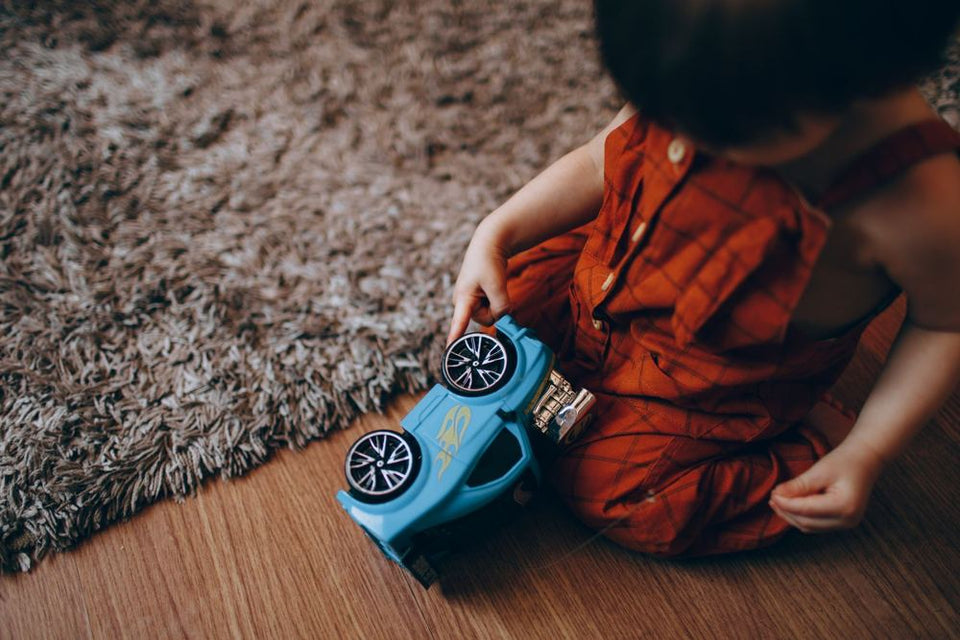 A child playing with a toy car on a rug