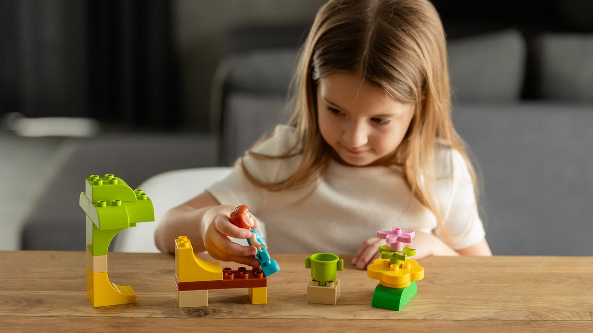 Young girl at a wooden table building small models from large chunky toy bricks